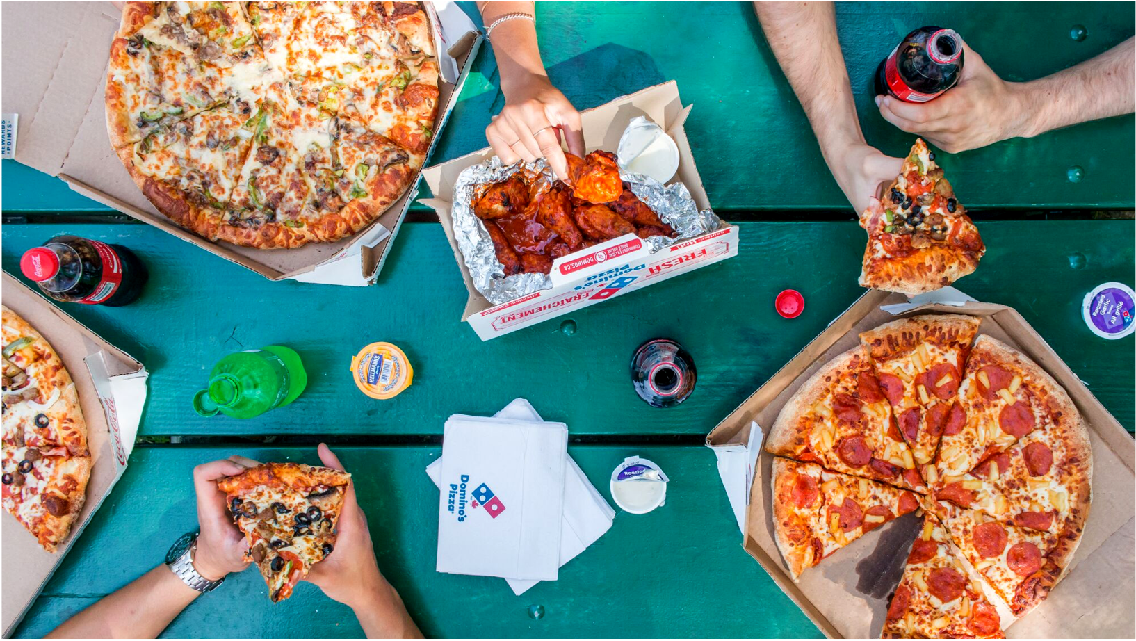 A picture taken from above showing people's hands sharing Domino's pizza and wings
