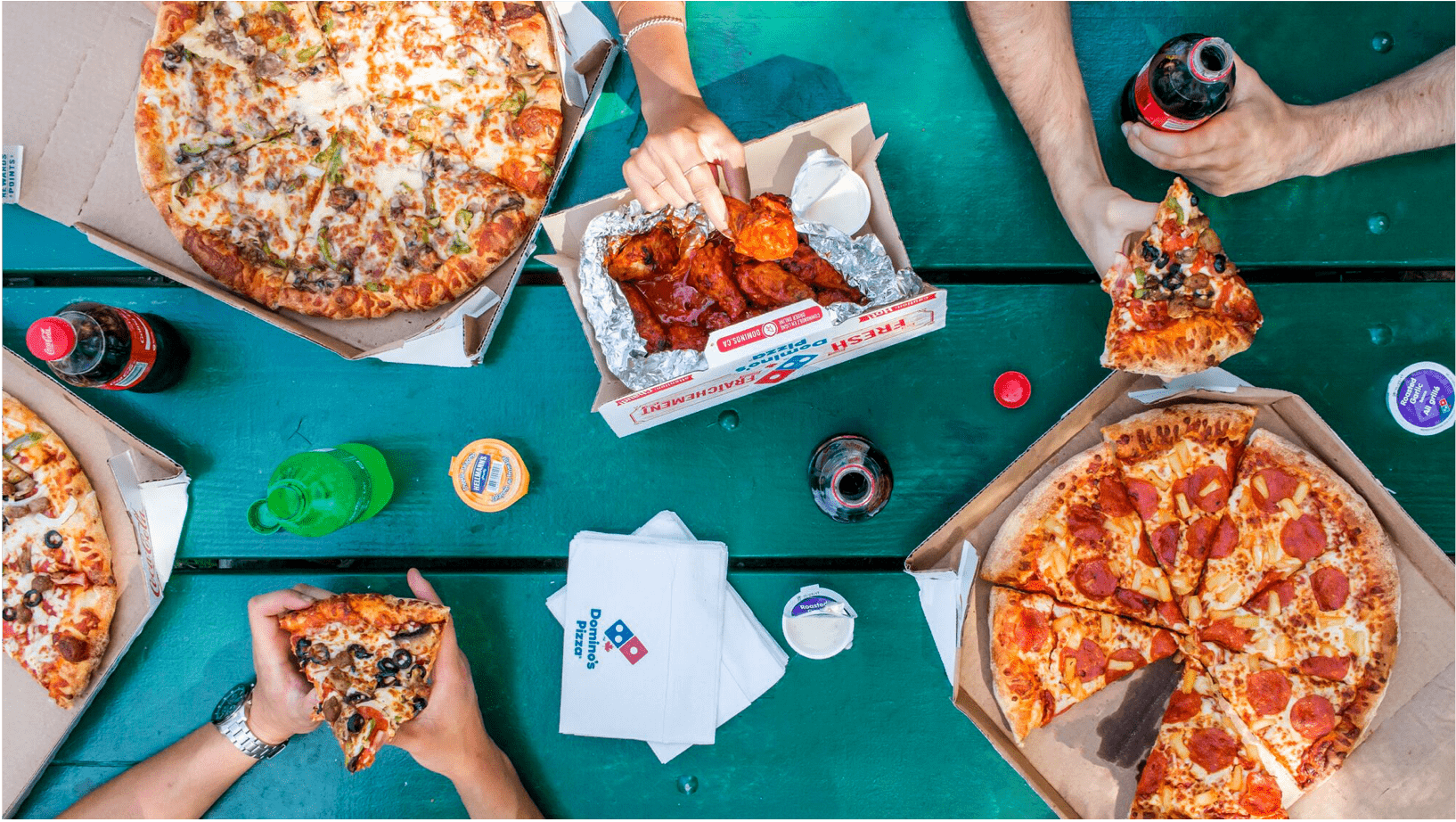 A picture taken from above showing people's hands sharing Domino's pizza and wings