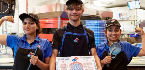 Three Domino's employees standing together, one holding a pizza box and the other two flexing