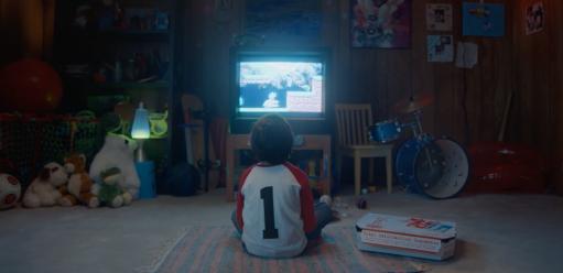 Photo of kid sitting in front of a TV playing a video game with a box of Domino's pizza next to him