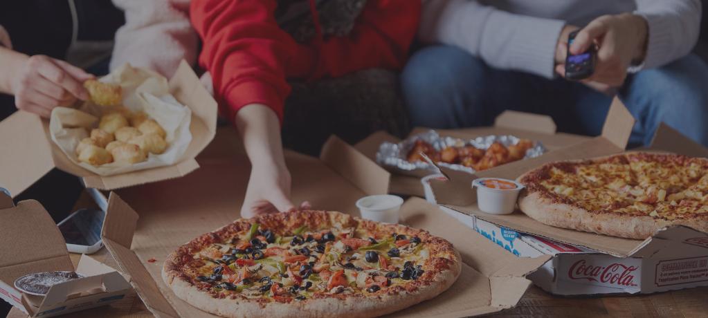 Several people sitting on a couch with opened boxes of Domino's pizza in front of them